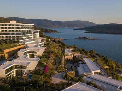 Moderne Hotelanlage am Hang mit Pool, grünen Gartenflächen und Blick auf das blaue Meer und Inseln.