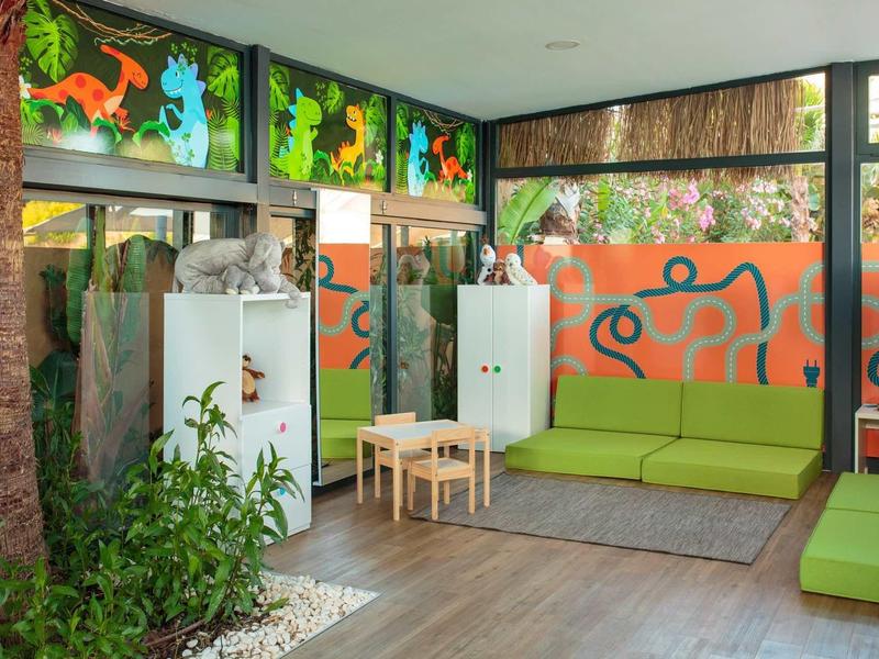 Světle zařízená čekárna se zelenými pohovkami a středně velkými bílými skříňkami.