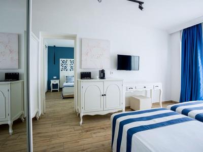 Lichte hotelkamer met twee eenpersoonsbedden, blauw-witte dekbedden en zicht op een aangrenzende kamer.