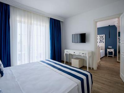Eenvoudig ingericht hotelkamer met tweepersoonsbed, tv en open deur naar een andere kamer.