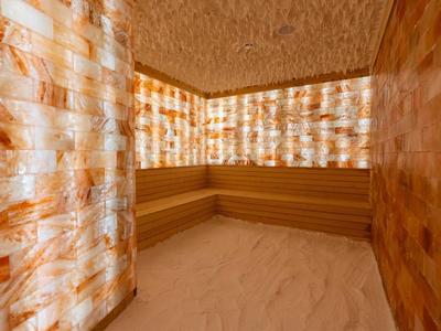 Een luxe spa ruimte met verlichte zoutsteenwanden en houten sauna zitplaatsen.