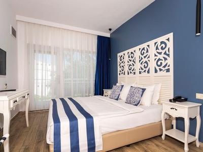 Lichte hotelkamer met tweepersoonsbed, blauwe accenten en gordijnen, houten vloer en moderne inrichting.