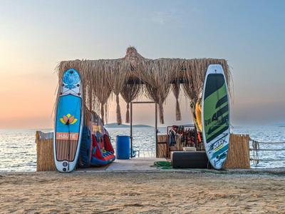Strandbar met rieten dak en twee surfplanken, zand en zee bij zonsondergang.