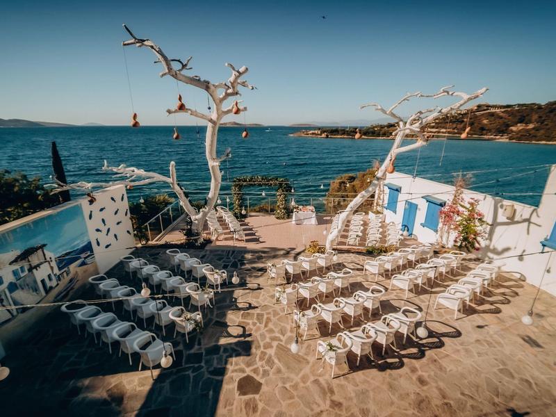 Terras met ligbedden en kale bomen met uitzicht op zee onder een heldere lucht.