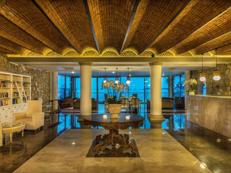 Elegante hotellobby met zuilen, kroonluchter en moderne verlichting bij schemering.