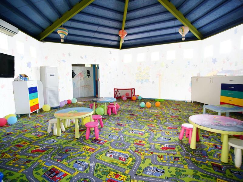 Heldere ronde speelruimte met kleurrijk tapijt en kleine tafels met stoelen.
