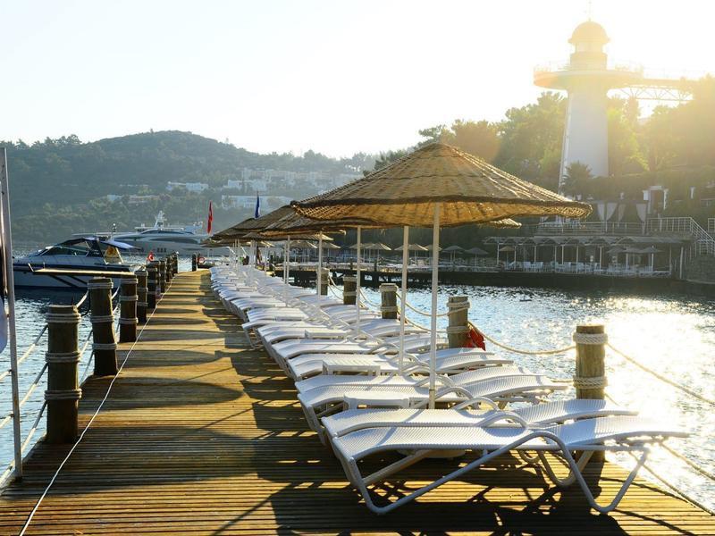 Steiger met ligstoelen en parasols naast water en heuvels op de achtergrond bij zonsondergang.