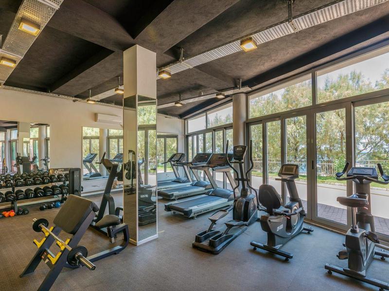 Moderne fitnessruimte met trainingsapparatuur en grote ramen met uitzicht op groen.