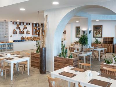 Area ristorante moderna e luminosa con tavoli bianchi, mobili in legno e piante sotto archi.