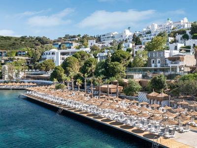 Spiaggia con lettini e ombrelloni davanti a edifici bianchi su una collina, acqua limpida.