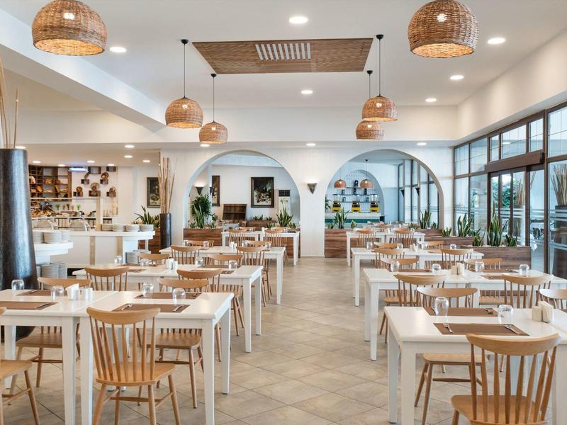 Jasna, nowoczesna jadalnia z drewnianymi krzesłami i stołami przy dużych oknach.