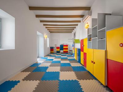 Lange, lichte kamer met kleurrijke kluisjes en zachte puzzelstukvormige vloerbedekking onder zichtbare balken.