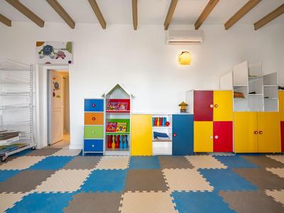 Heldere speelkamer voor kinderen met kleurrijke opbergkasten, boekenplanken en blauw-beige geruite vloermatten.