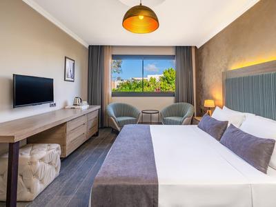 Modernes Hotelzimmer mit Doppelbett, zwei Sesseln, Schreibtisch und großem Fenster mit Ausblick.