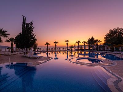 Poolbereich eines Hotels mit Palmen und Liegestühlen bei Sonnenuntergang.