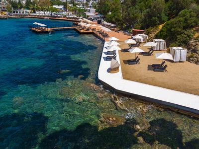 Klares Meerwasser neben einer stilvollen Hotelterrasse mit Liegestühlen und Sonnenschirmen.