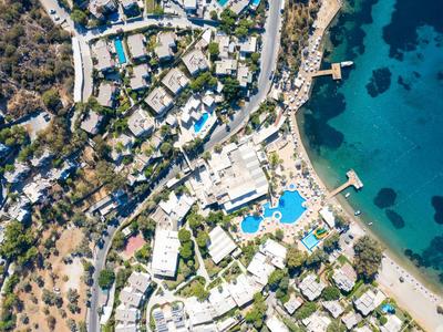 Luchtfoto van een kustresort met zwembaden, witte gebouwen en helderblauwe zee.