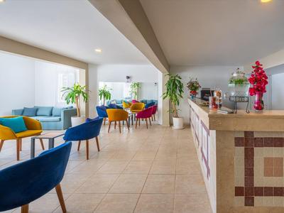 Lichte hotelhal met kleurige stoelen, grote ramen en betegelde balie.