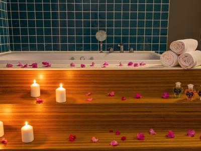 Wellnessbad met houten treden, brandende kaarsen, rozenblaadjes en opgerolde handdoeken voor een ontspannen sfeer.