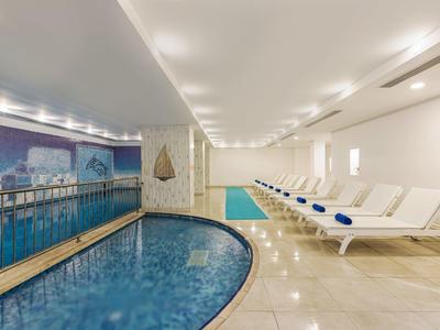 Overdekt zwembad met ligstoelen en kustmuurschildering in een lichte, moderne ruimte.