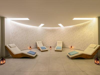 Moderne spa ontspanningsruimte met gebogen muur en vijf ligstoelen met kussens en lantaarns.