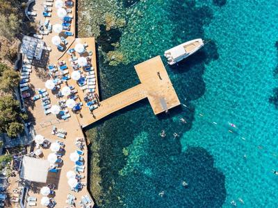 Luchtfoto van een aanlegsteiger met ligstoelen en parasols langs de rotsachtige kust bij helder blauw water.