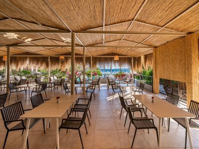Ruim buitenterras met houten tafels, stoelen en een dak van riet.