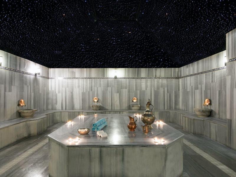 Buiten marmeren Turks bad met kaarsen en beelden onder een sterrenhemel.