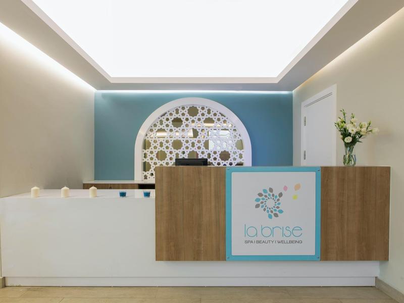 Moderne hotelreceptie met een houten en wit bureau, blauwe accentmuur en decoratieve cirkelvormige wandkunst.