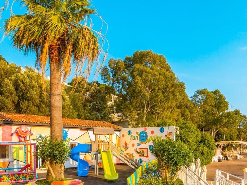 Kleurrijke speeltuin met palmbomen en heldere blauwe lucht nabij een strandgebied.