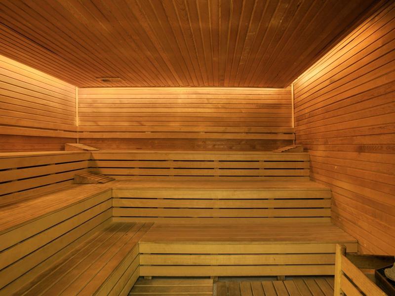 Houten sauna met trapvormige banken en warme verlichting langs het plafond.