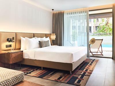 Modernes Hotelzimmer mit großem Bett, Nachttischen und Zugang zu einem Balkon mit Sitzgelegenheit.