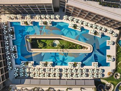 Vogelperspektive eines Hotels mit großem rechteckigem Pool und vielen Sonnenschirmen.