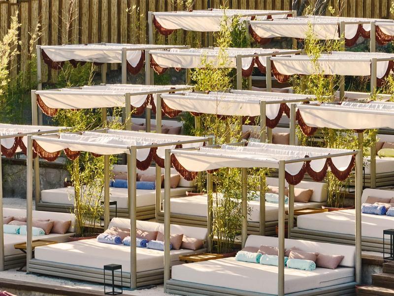 Außenliegende bequeme Doppelbetten mit Baldachinen und Kissen, umgeben von Pflanzen und Holzzäunen.