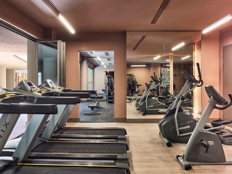 Helles Fitnessstudio mit Laufbändern, Fahrrädern, Spiegelwand und Holzfußboden.