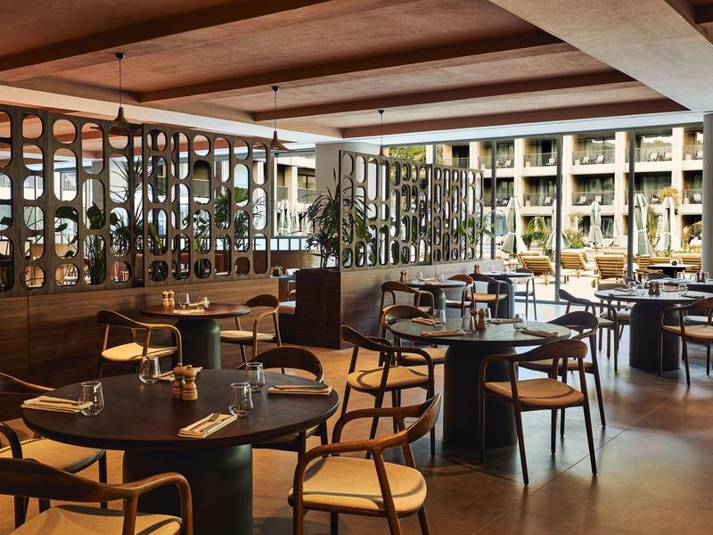 Modernes Restaurant mit Holztischen, Stühlen, großen Fenstern und gemütlicher Beleuchtung.