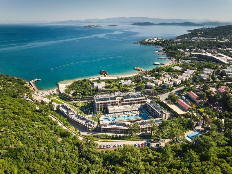 Blick auf eine Küstenstadt mit blauem Meer, Strand, grünen Hügeln und mehreren Gebäuden.