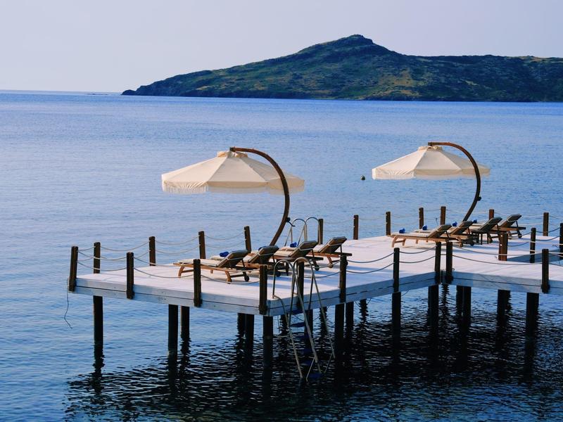 Molo con lettini e ombrelloni sopra acqua calma con un'isola sullo sfondo