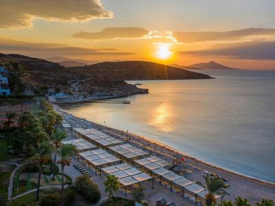Sunset over a beach with loungers and shaded cabanas beside a calm sea.
