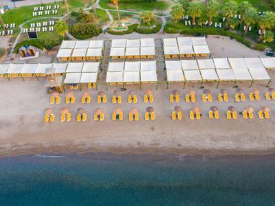 Aerial view of a beach with yellow sunshades and a large beach club with white canopies.