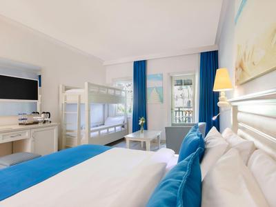 Bright hotel room with double bed, bunk bed, TV, and blue-white decor.