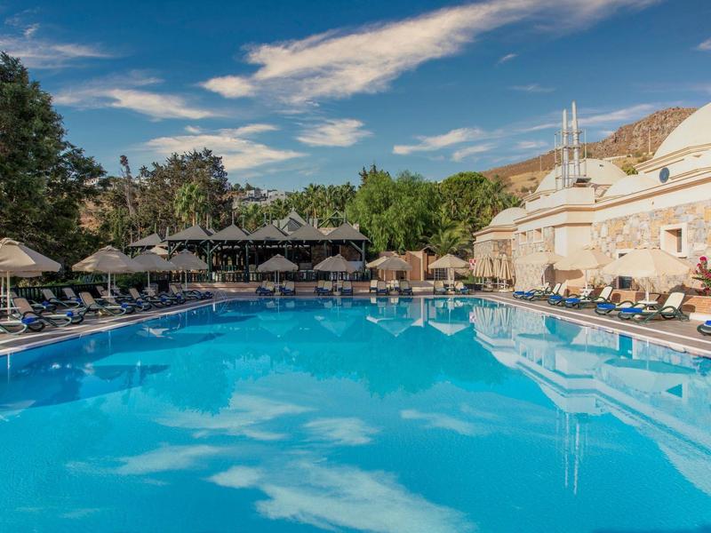Large outdoor pool with lounge chairs and umbrellas under a blue sky at a hotel.