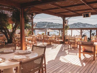 Ristorante aperto con pavimento in legno e vista sull'acqua e sulle montagne sullo sfondo.