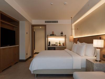 Camera d'hotel moderna con grande letto, illuminazione calda e TV a parete.