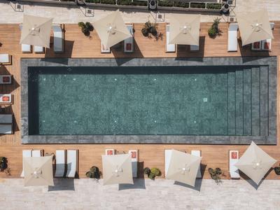 Vista aerea di una piscina rettangolare con lettini e ombrelloni su un ponte in legno.