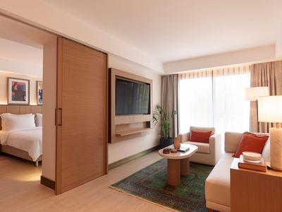 Camera d'hotel moderna con zona giorno, divano, TV e camera da letto adiacente con letto grande.