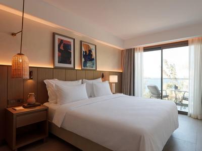 Camera d'hotel luminosa con letto matrimoniale, lampade da comodino e balcone con vista.