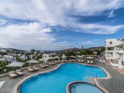 Grande piscina dell'hotel con lettini e ombrelloni sotto un cielo blu in un villaggio turistico.