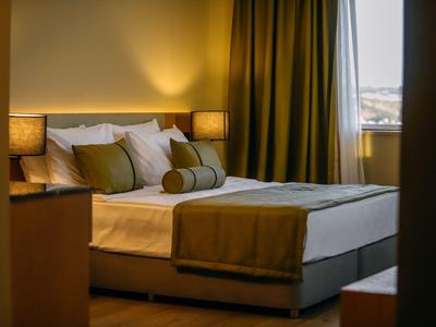 Gemütliches Doppelbett mit grüner Bettdecke und Kissen in ruhigem Hotelzimmer mit Lampe.