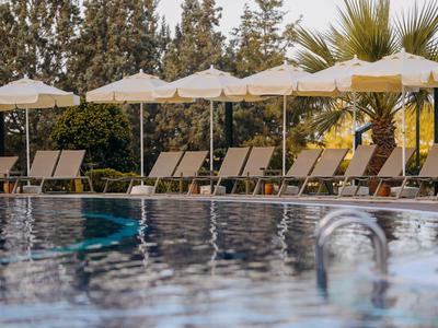 Pool mit Liegestühlen und weißen Sonnenschirmen, umgeben von Bäumen und Palmen.